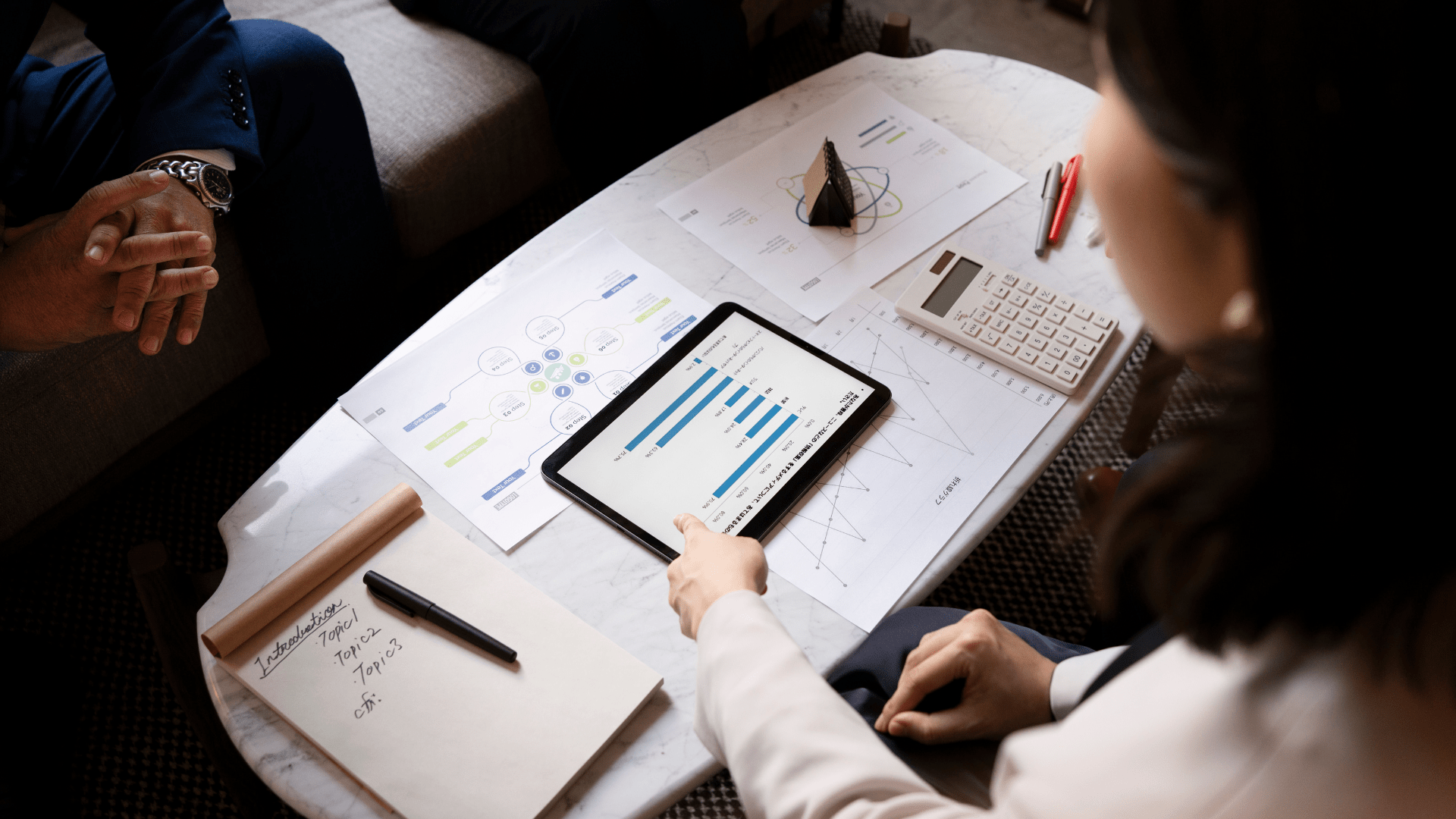 Person pointing at tablet displaying charts and data analysis, surrounded by documents and a calculator, illustrating strategies for optimizing rental listings and increasing bookings.